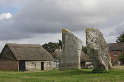 two huge prehistoric standing stones in front of a thatched building